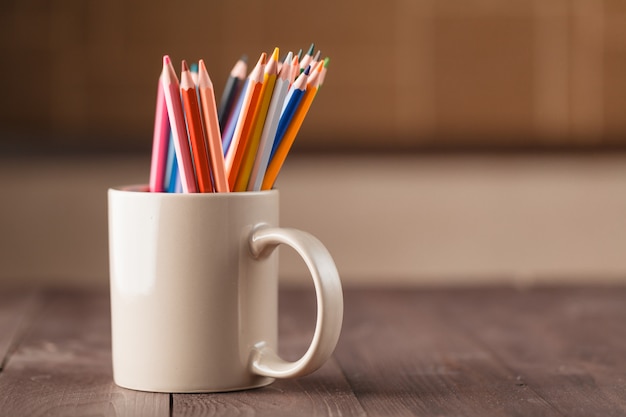 Many pencils in mug on wooden table