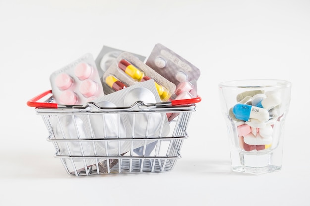 Many pills pack in the shopping cart and glass on white background