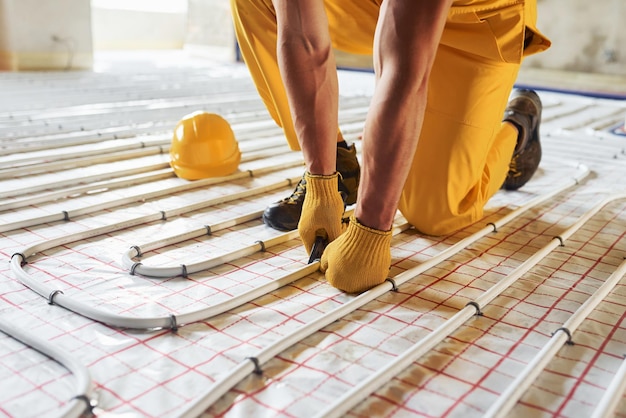 Many of pipes Worker in yellow colored uniform installing underfloor heating system