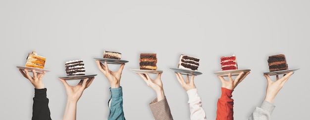 Many plates with pieces of different cakes in the hands of the waiters who lifted them up