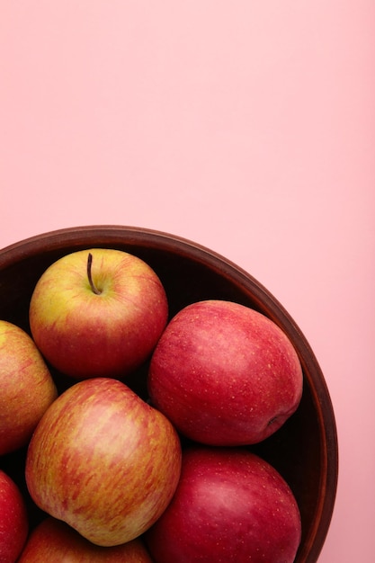 Many red apples in round bowl on pink background Vertical photo