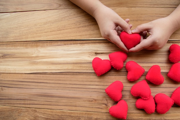 Many red hearts and boy hands hold red heart on wooden background