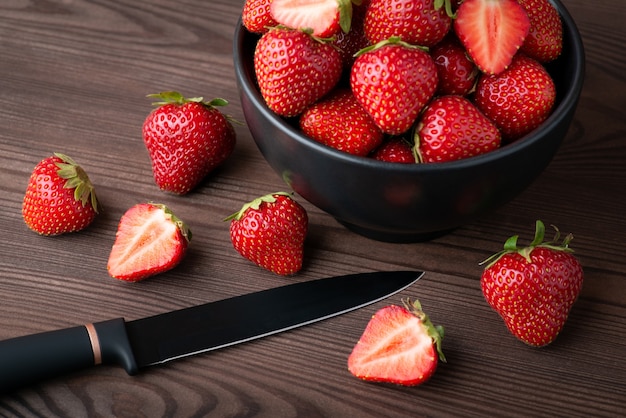 many ripe strawberry in the bowl on a black wooden background