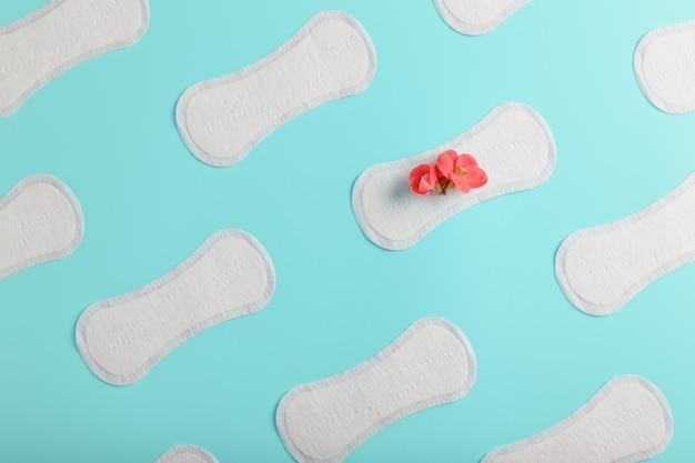 Many Sanitary pads on a blue background in the form of a diagonal pattern with a flower. Textured background all over the screen.