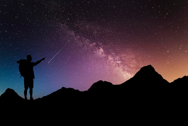 Many stars milky way and silhouette offor a traveling man\
standing alone on top of a mountain