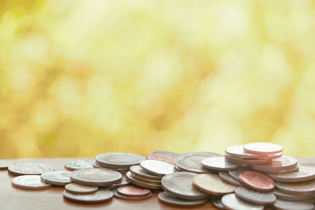 Many Thai coins on wooden table on bokeh yellow brown color tone