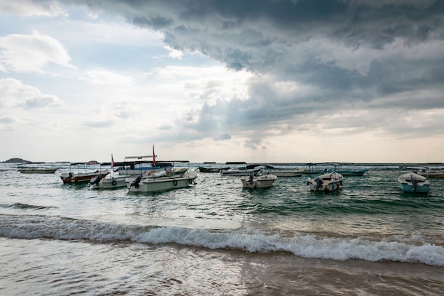 Многие традиционные лодки и яхты у моря или океана. Надвигающаяся тропическая буря с дождем и темными дождевыми облаками в небе и прорывающимся солнцем