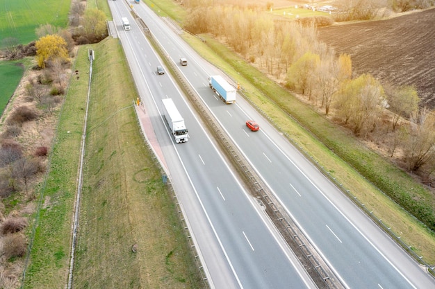 Many trucks are moving along the highway crossing road between the fields drone view