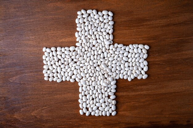 Many white beans poured into the shape of a cross on a wooden background