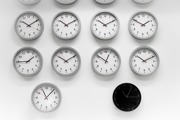 Many White clock and a black classic round wall clock. Different concepts of time