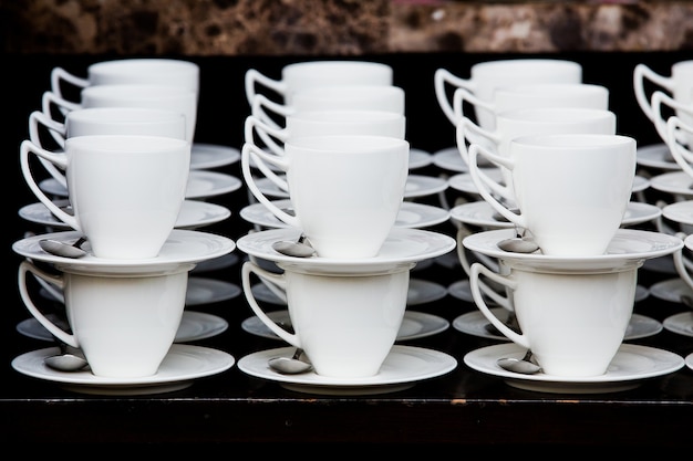 Many white coffee cups in a line over a buffet