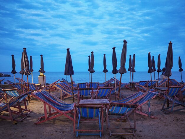 Many wooden deckchairs and umbrellas on sand at sunset beach. 