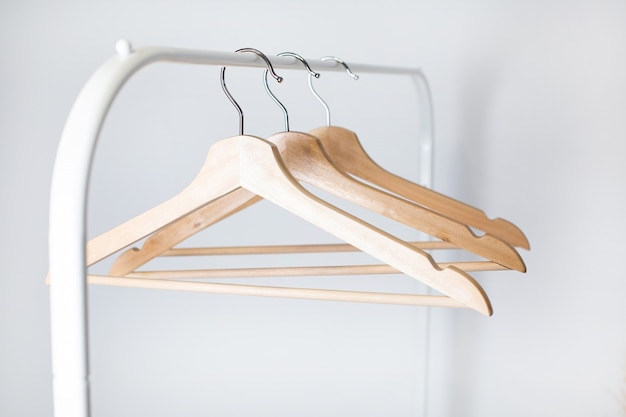 Many wooden hangers on a rod, isolated on white wall background.