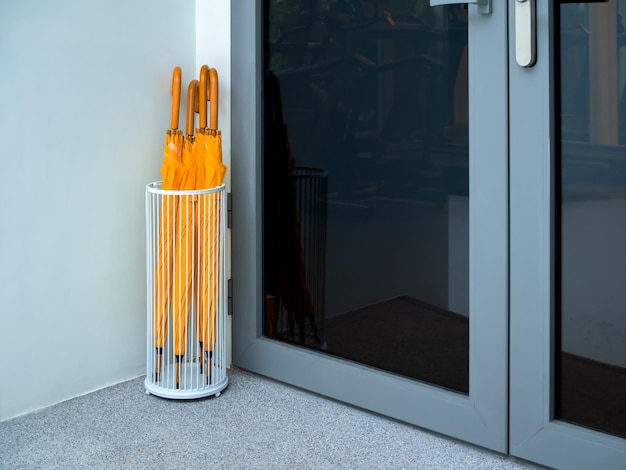 Many yellow umbrellas with wooden handle stored in white vintage steel umbrella storage in front of the glass door of the building