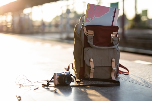 Map in backpack mobile phone with earphone and hat at the train\
station with a travelersun set tr