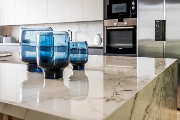 Marble island detail of a large kitchen with stainless steel appliances and decorative blue glass vases