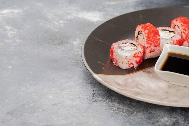 Piatto in marmo di involtini di sushi california e salsa di soia su pietra.