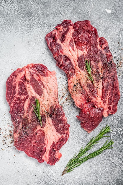 Marbled raw meat steaks cooking with seasonings and olive oil\
fresh beef rib eye steaks white background top view