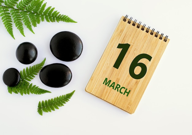 March 16 16th day of the month calendar date Notepad black stones green leaves Spring month the concept of the day of year