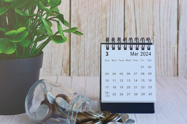Календарь на стол с стопом монет и горшечным растением на деревянном столе