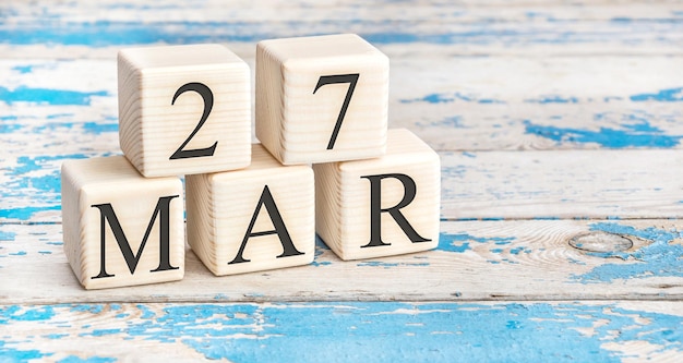 March 27th. Wooden cubes with date of 27 March on old blue wooden background.