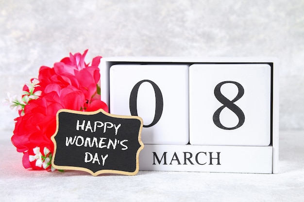 March 8, International Women's Day. Wooden perpetual calendar, pink flowers and chalkboard.