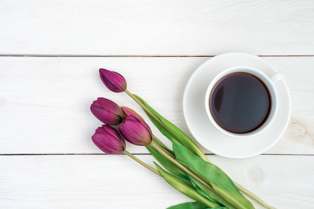 March 8, tulips and coffee in a white cup on a light wooden background.