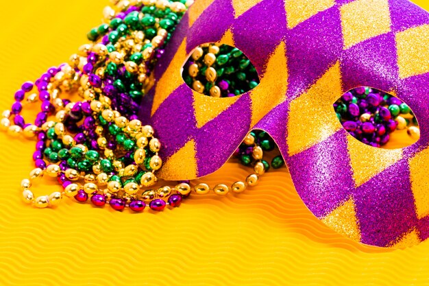 Mardi Gras beads and mask on yellow backgound.