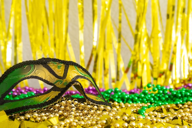 Mardi gras mask closeup and purple gold green beads on gold background.