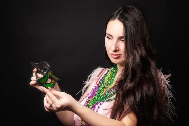 Mardi gras people. Woman holds a carnival mask and beads on the black background.