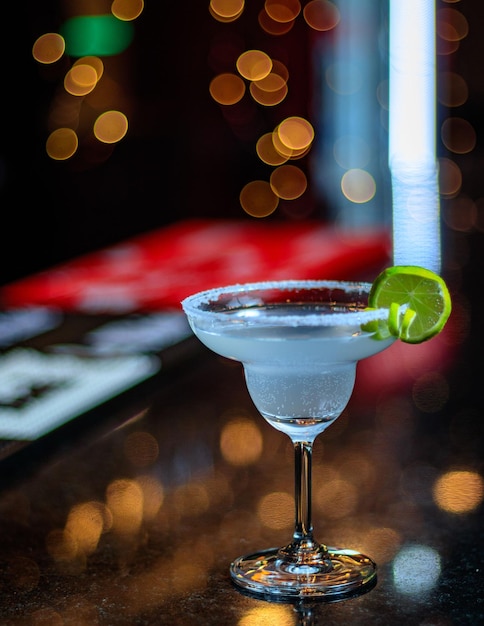 A margarita glass with a lime wedge on the rim sits on a bar counter.