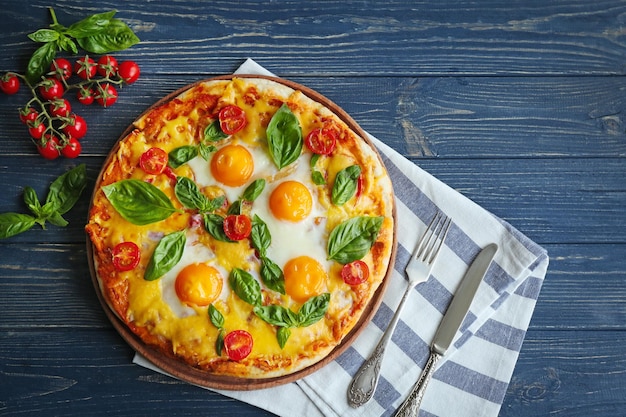 Margarita pizza with basil leaves and egg on wooden table top view