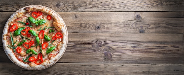 Margherita pizza with red pepper and fresh basil on a wooden table