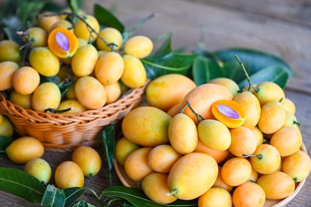 Marian pruim fruit en bladeren in mand op houten achtergrond tropisch fruit naam in thailand sweet yellow marian plum maprang plango of mayong chid