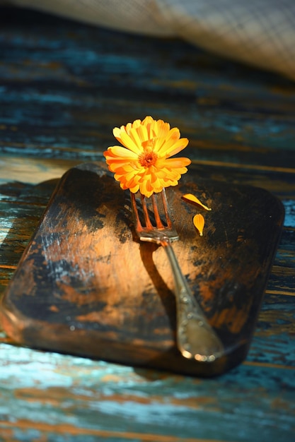 Marigold flower on antique fork on burnedout kitchen board on rough dyed table