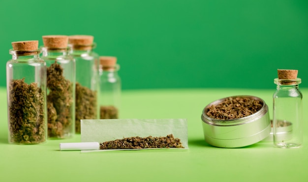 marijuana cigar with grinder glass jars on green table with dark green background