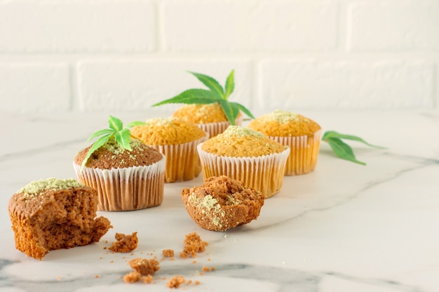 Marijuana cupcake muffins and cannabis leaves on a white marble table. Home cooked.