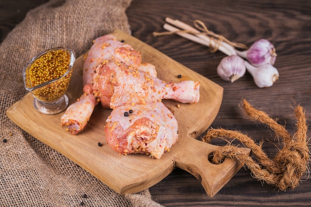 Marinated chicken legs with raw potatoes and garlic on rustic wooden table. Preparing food or cooking concept.