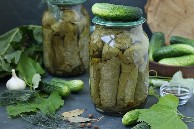 Marinated cucumbers in grape leaves with garlic and dill in two glass jars on a dark background