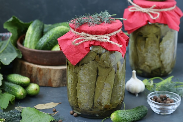 Marinated cucumbers in grape leaves with garlic and dill in two glass jars on a dark surface, Horizontal format, Closeup