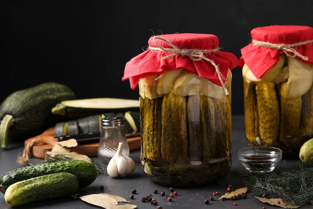 Marinated cucumbers and zucchini in jars on dark