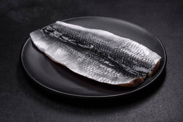 Marinated fillet with spices and herbs of sea herring on a black plate