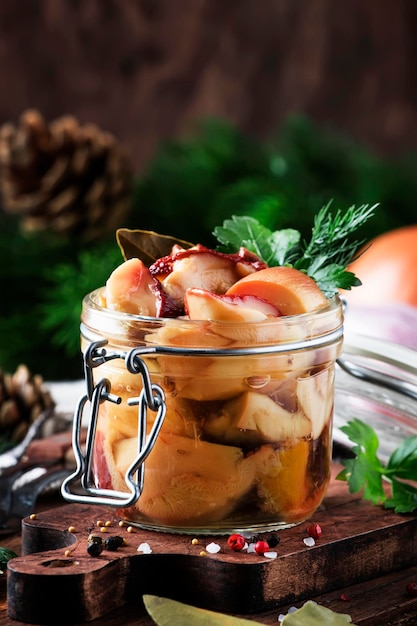 Porcini di funghi bianchi di foresta marinati in barattolo di vetro con spezie ed erbe aromatiche pronte da mangiare per cucinare cibo o concetto di conserve tavolo da cucina in legno spazio copia stile rustico fuoco selettivo