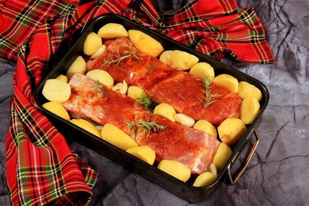 Маринованная свежая свиная грудинка с красным перцем, розмарином, специями и овощами в металлической сковороде