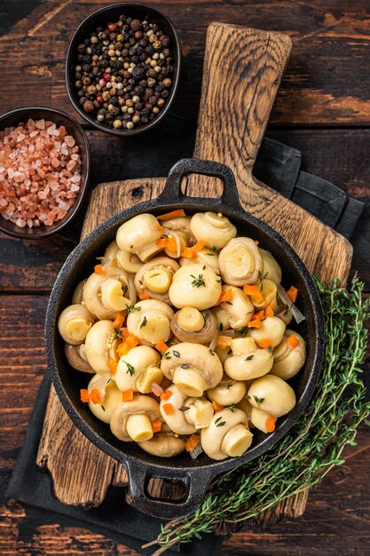 Marinated mushrooms champignons in a pan. Dark Wooden background. Top view.