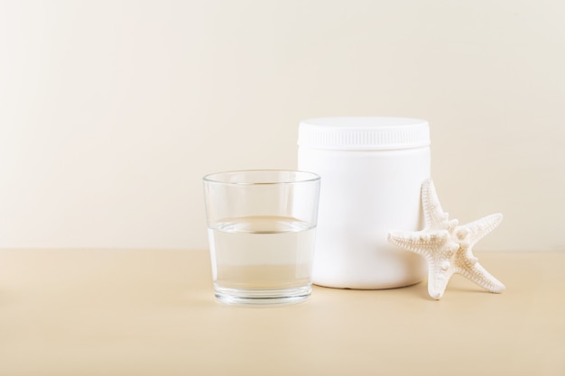 marine collagen in a white jar a glass of water beige background