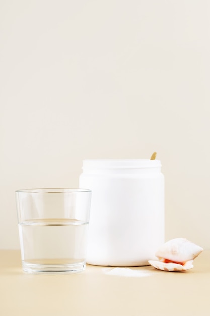 marine collagen in a white jar a glass of water beige background