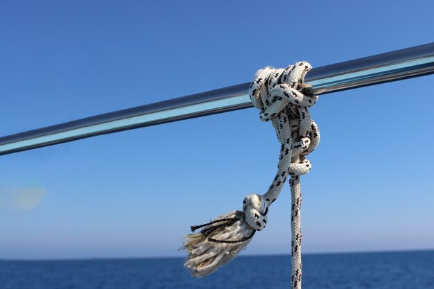 Photo marine knot detail stainless steel boat railing. marine fender knot around boat lee. close-up nautical knot rope on sail boat.