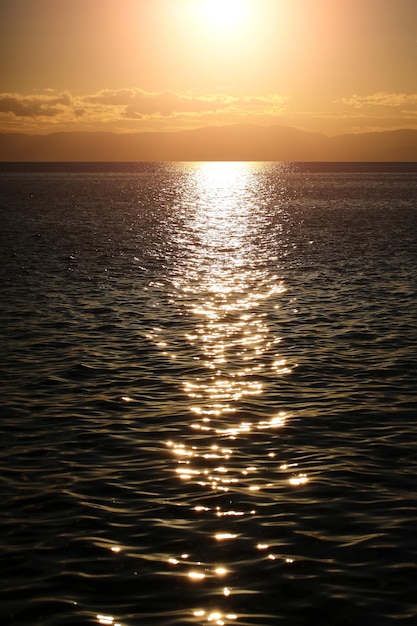 Marine sunset scene with lights reflecting at dark seaways in foreground and sun with halo glade shi...