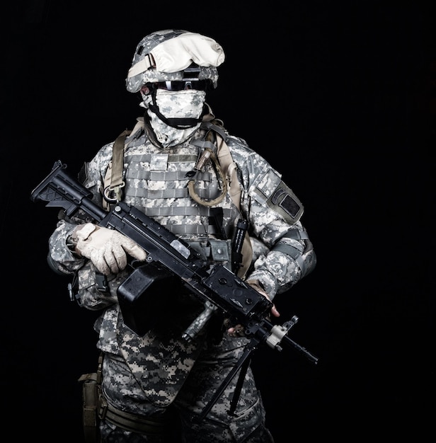 Marine with hiding identity, protected with helmet and body armour in digital camouflage combat uniform posing with light machine gun equipped infrared laser aiming light isolated on black background